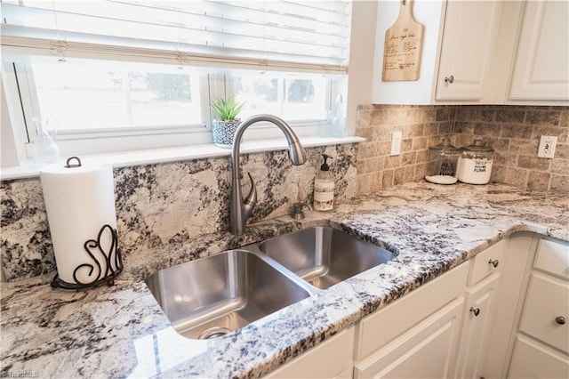 kitchen view of a sink, light stone counters, decorative backsplash, and white cabinets