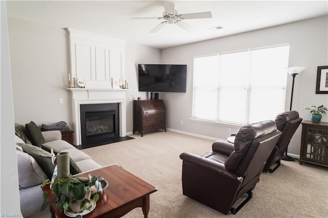 living area with light colored carpet, a fireplace with flush hearth, ceiling fan, and baseboards