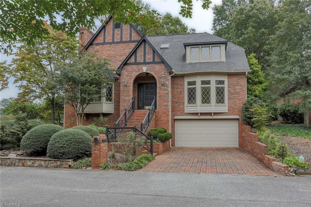 tudor house with brick siding, decorative driveway, a shingled roof, and a garage