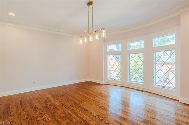 spare room with wood finished floors, visible vents, baseboards, and ornamental molding
