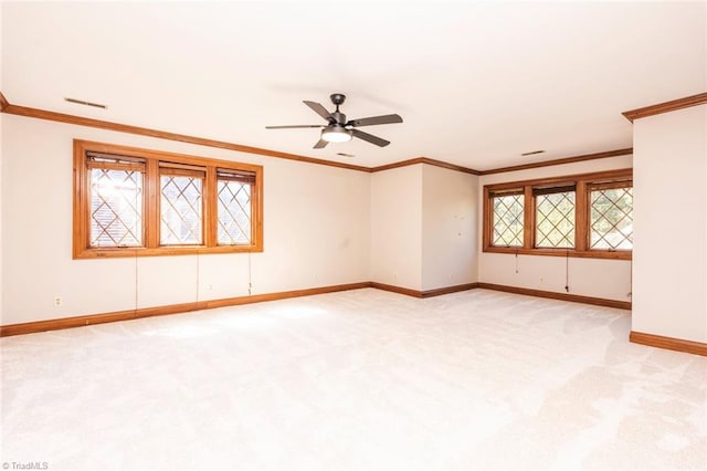 empty room featuring visible vents, a ceiling fan, light carpet, crown molding, and baseboards