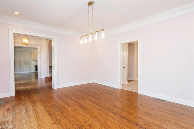 spare room featuring baseboards, wood finished floors, visible vents, and ornamental molding