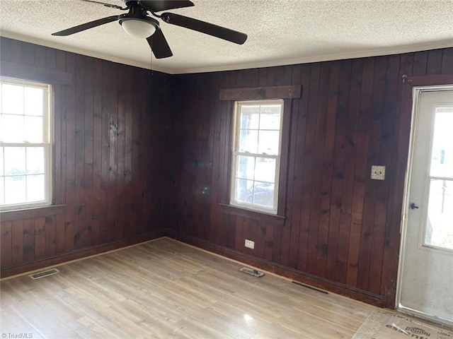 unfurnished room featuring a textured ceiling, ceiling fan, crown molding, wooden walls, and light hardwood / wood-style flooring