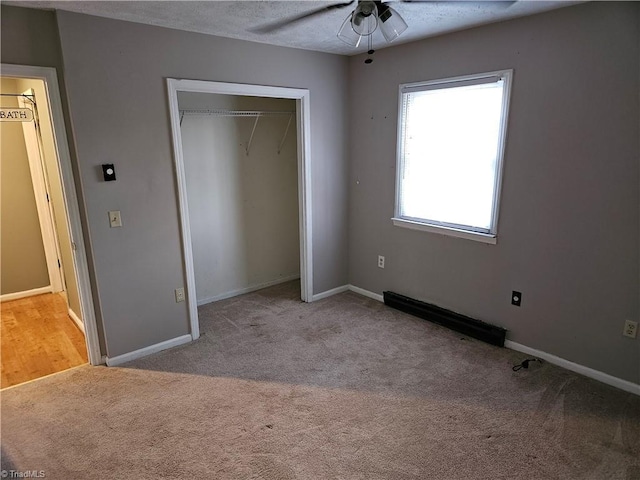 unfurnished bedroom featuring light colored carpet, baseboard heating, ceiling fan, a textured ceiling, and a closet