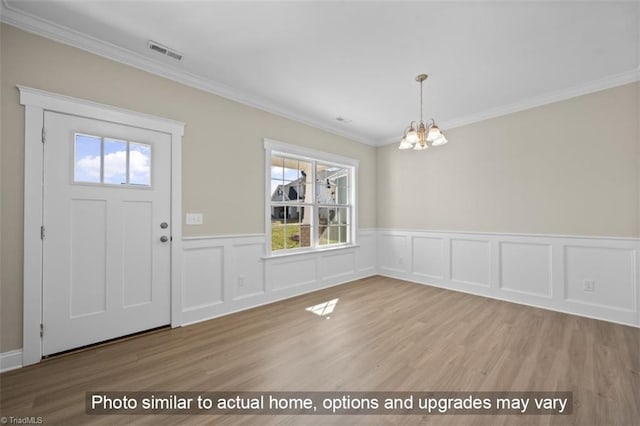 foyer entrance featuring an inviting chandelier, plenty of natural light, light wood-type flooring, and ornamental molding