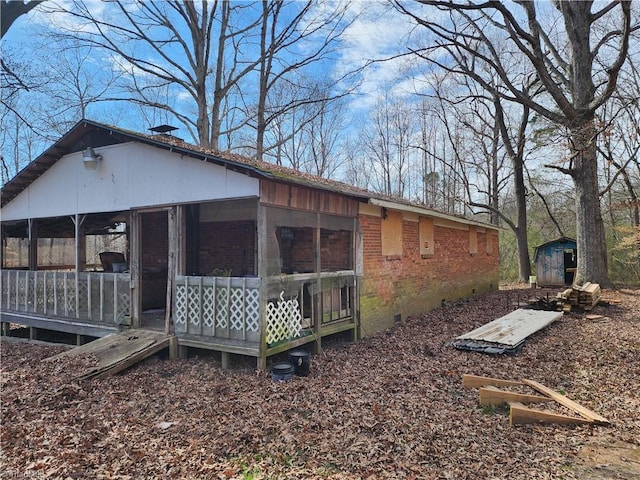 view of side of home featuring a sunroom, crawl space, brick siding, and a storage unit