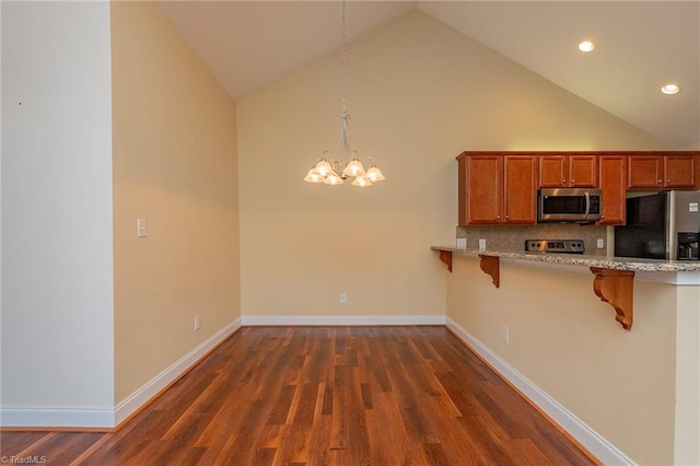 kitchen with a kitchen breakfast bar, dark wood-type flooring, brown cabinets, a chandelier, and stainless steel appliances