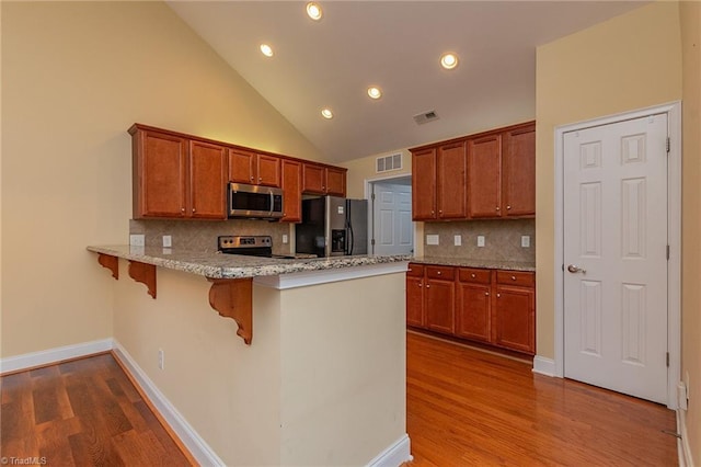 kitchen featuring visible vents, a peninsula, appliances with stainless steel finishes, and brown cabinets