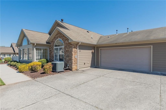 single story home featuring roof with shingles, central AC, concrete driveway, an attached garage, and stone siding