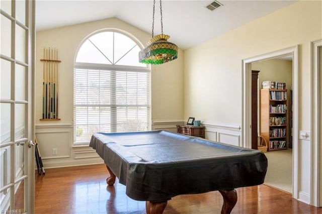 recreation room with a decorative wall, a wainscoted wall, wood finished floors, vaulted ceiling, and visible vents