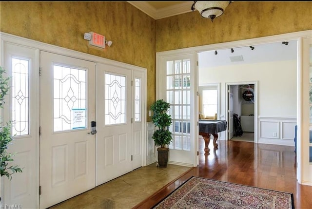foyer entrance with visible vents, ornamental molding, a decorative wall, wood finished floors, and french doors