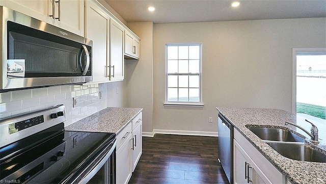 kitchen with light stone countertops, appliances with stainless steel finishes, dark wood-type flooring, sink, and white cabinetry