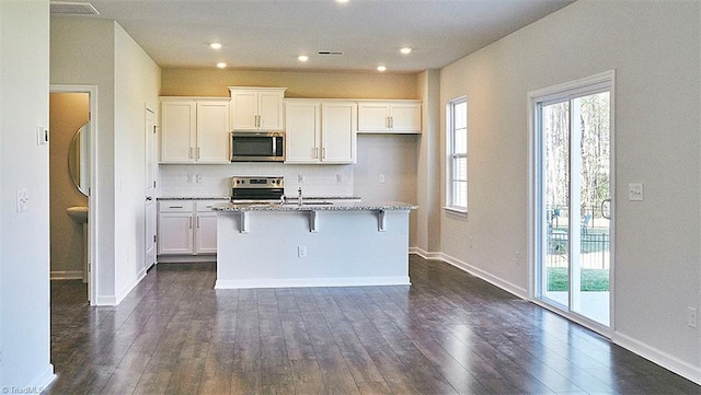 kitchen with a center island with sink, stainless steel appliances, light stone countertops, and white cabinetry