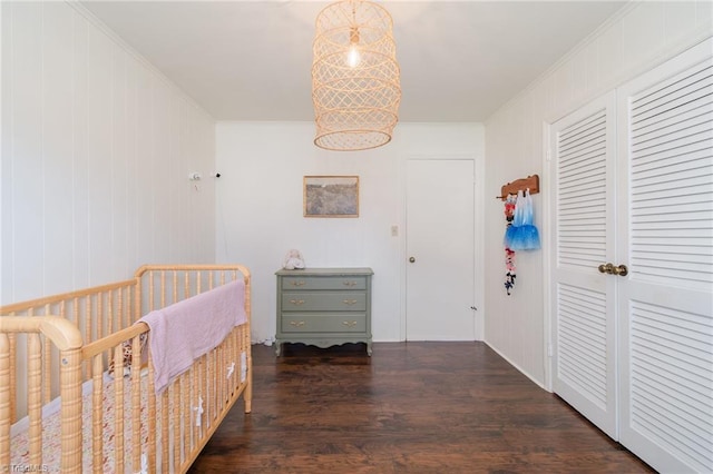 bedroom with a nursery area, a closet, ornamental molding, and wood finished floors