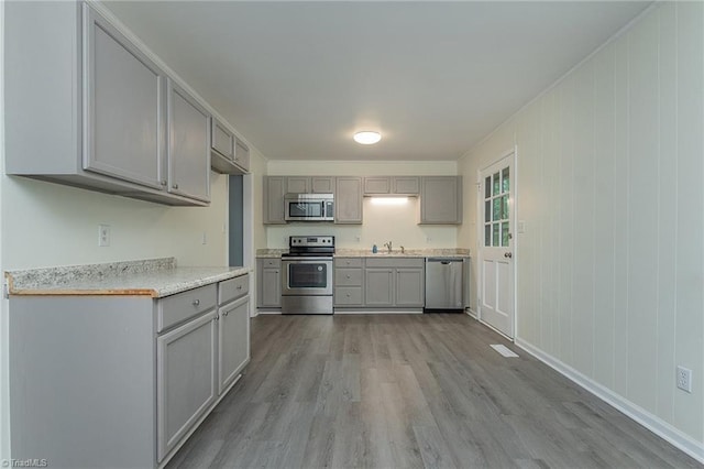kitchen with wood finished floors, gray cabinetry, light countertops, and appliances with stainless steel finishes