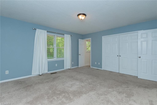 unfurnished bedroom featuring a closet, a textured ceiling, baseboards, carpet flooring, and visible vents