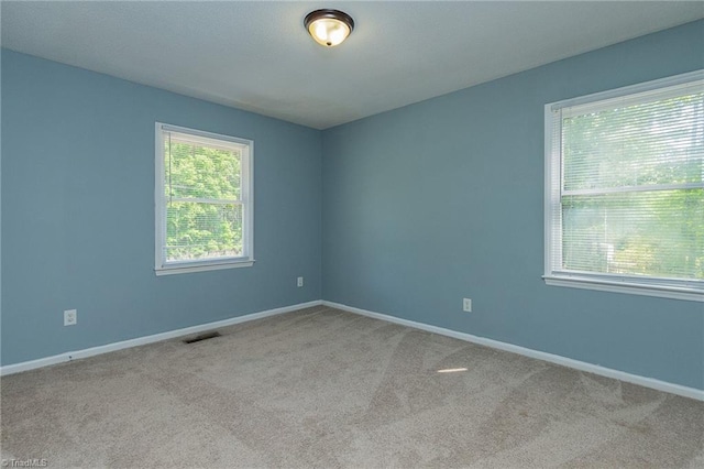 carpeted empty room with baseboards, plenty of natural light, and visible vents