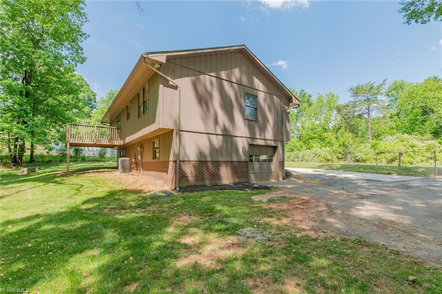 view of home's exterior featuring central air condition unit, a deck, an attached garage, driveway, and a lawn