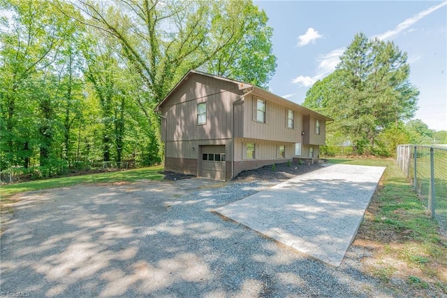 view of side of property with fence, a garage, brick siding, and gravel driveway