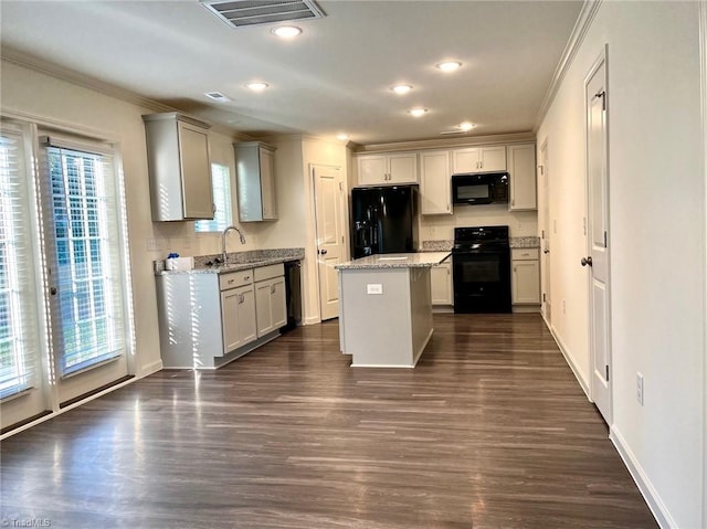 kitchen featuring visible vents, a kitchen island, a sink, black appliances, and dark wood-type flooring