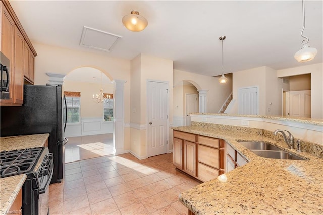 kitchen featuring black gas range, decorative light fixtures, light stone counters, and sink