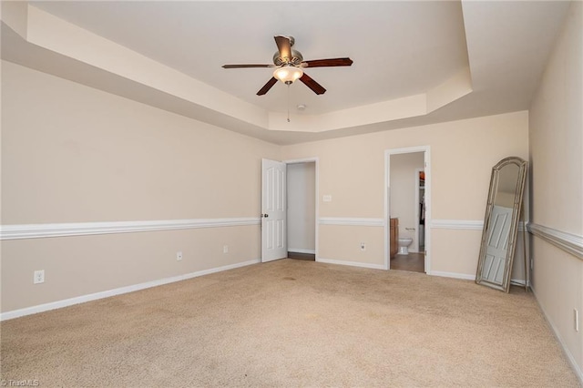 unfurnished bedroom with a tray ceiling, light carpet, ceiling fan, and a spacious closet