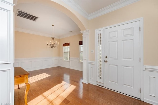 entrance foyer featuring ornate columns, hardwood / wood-style floors, a notable chandelier, and ornamental molding