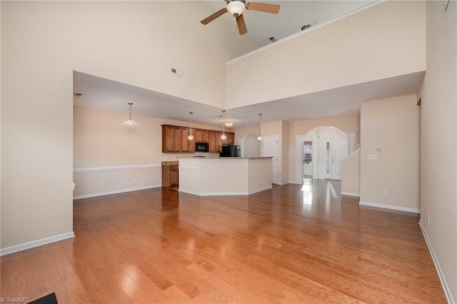 unfurnished living room with light wood-type flooring, a towering ceiling, and ceiling fan