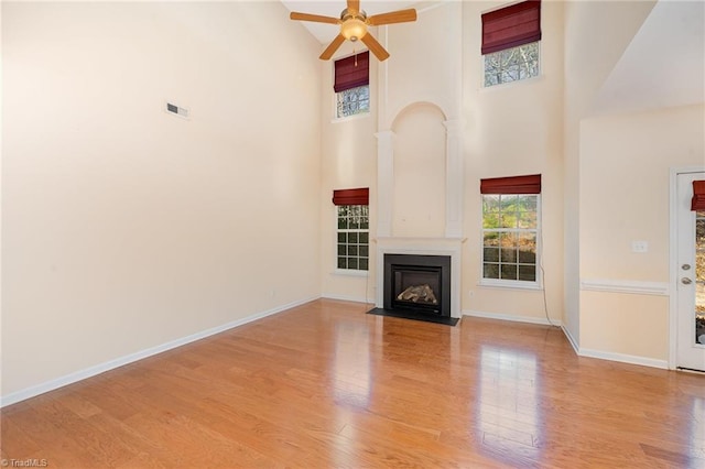 unfurnished living room featuring light wood-type flooring, a towering ceiling, a large fireplace, and ceiling fan