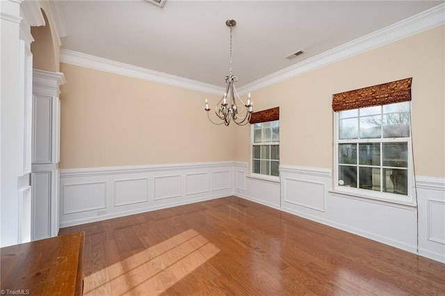 unfurnished dining area featuring wood-type flooring, crown molding, and an inviting chandelier