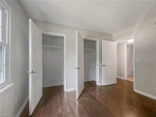 unfurnished bedroom with dark hardwood / wood-style flooring and two closets