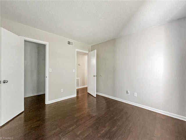 unfurnished bedroom featuring dark hardwood / wood-style flooring, a spacious closet, a textured ceiling, and a closet