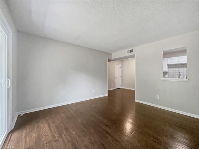 spare room featuring a textured ceiling and dark wood-type flooring