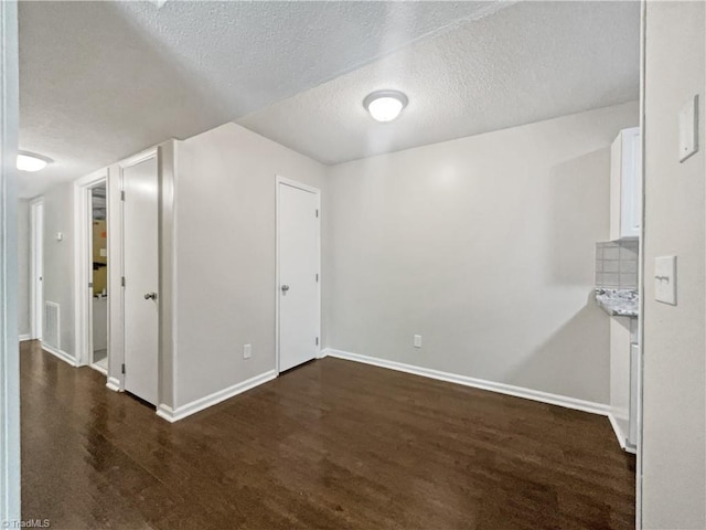 spare room with a textured ceiling and dark hardwood / wood-style flooring