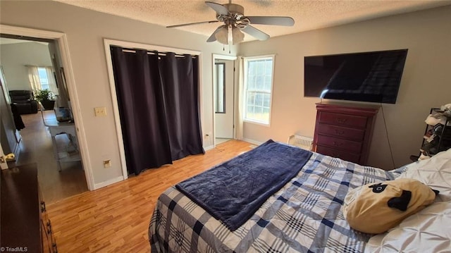 bedroom with radiator heating unit, baseboards, a textured ceiling, and light wood finished floors