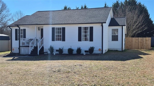 view of front facade featuring a shingled roof, fence, and a front yard