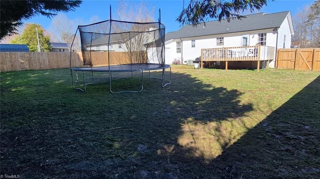 view of yard with a trampoline, a wooden deck, and a fenced backyard