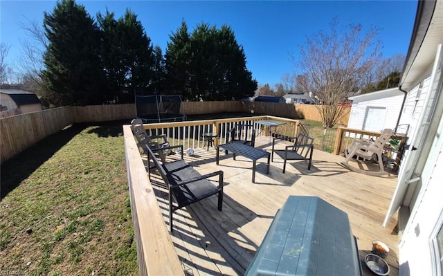 wooden deck featuring a fenced backyard, a trampoline, and a yard