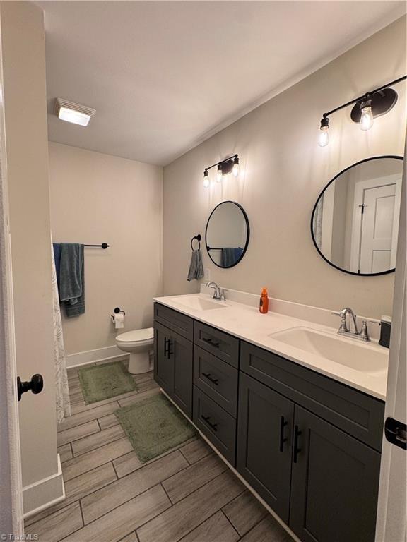 3064 Wesley Farm Ln, Sophia, NC 27350 - bathroom with wood tiled floors, toilet, double vanity, and baseboards