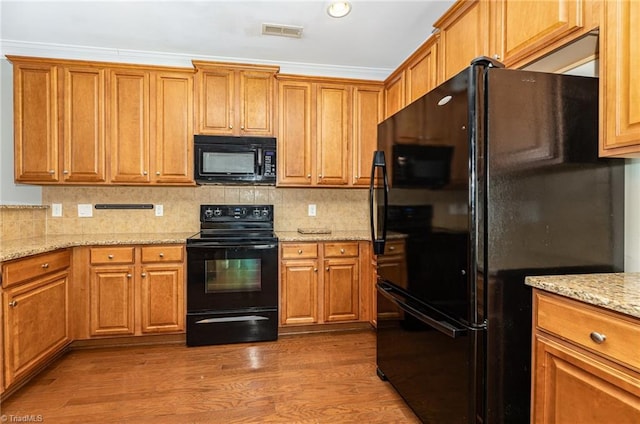 kitchen with black appliances, crown molding, dark hardwood / wood-style flooring, light stone counters, and tasteful backsplash