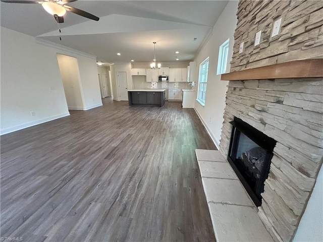 unfurnished living room with ceiling fan, dark hardwood / wood-style floors, ornamental molding, a stone fireplace, and vaulted ceiling