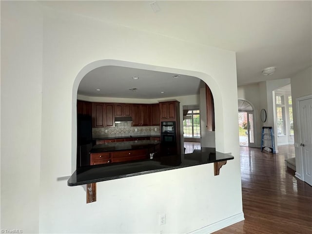 kitchen with decorative backsplash, a kitchen bar, kitchen peninsula, dark wood-type flooring, and black appliances