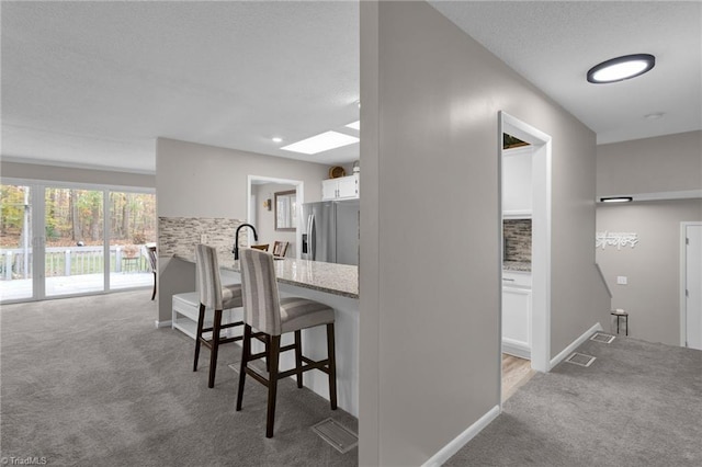 kitchen featuring light colored carpet, stainless steel fridge with ice dispenser, a breakfast bar area, and white cabinets