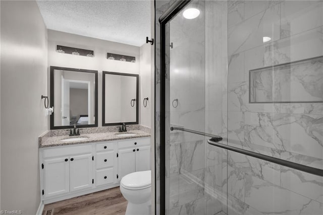 bathroom featuring hardwood / wood-style floors, vanity, walk in shower, toilet, and a textured ceiling