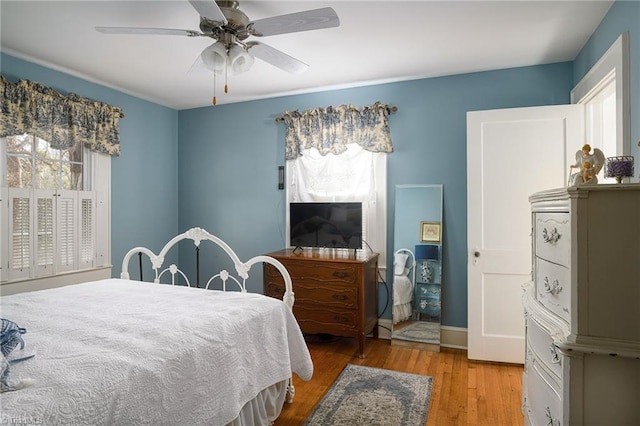 bedroom featuring a ceiling fan, multiple windows, wood finished floors, and baseboards