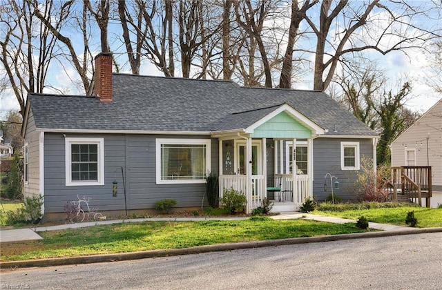 view of front facade with a front yard, roof with shingles, and a chimney