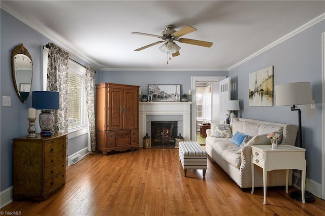 living room with a ceiling fan, wood finished floors, a lit fireplace, crown molding, and baseboards
