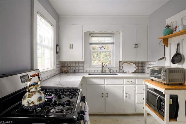 kitchen with stainless steel gas range oven, backsplash, black microwave, a toaster, and a sink