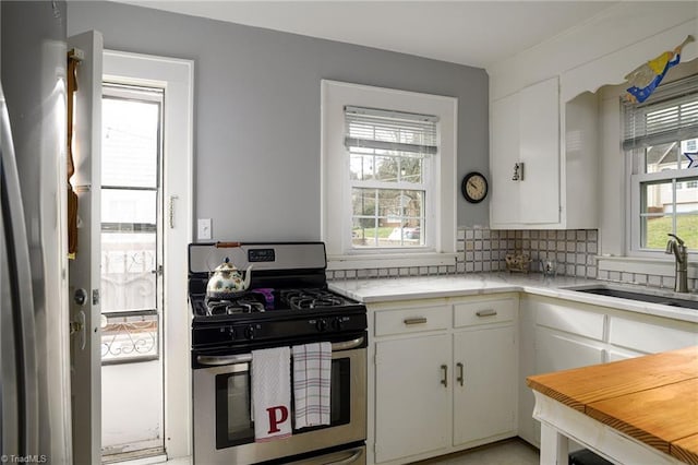 kitchen featuring a sink, backsplash, white cabinets, light countertops, and gas range