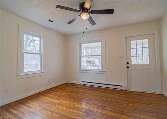 interior space with a baseboard heating unit, a wealth of natural light, wood-type flooring, and visible vents